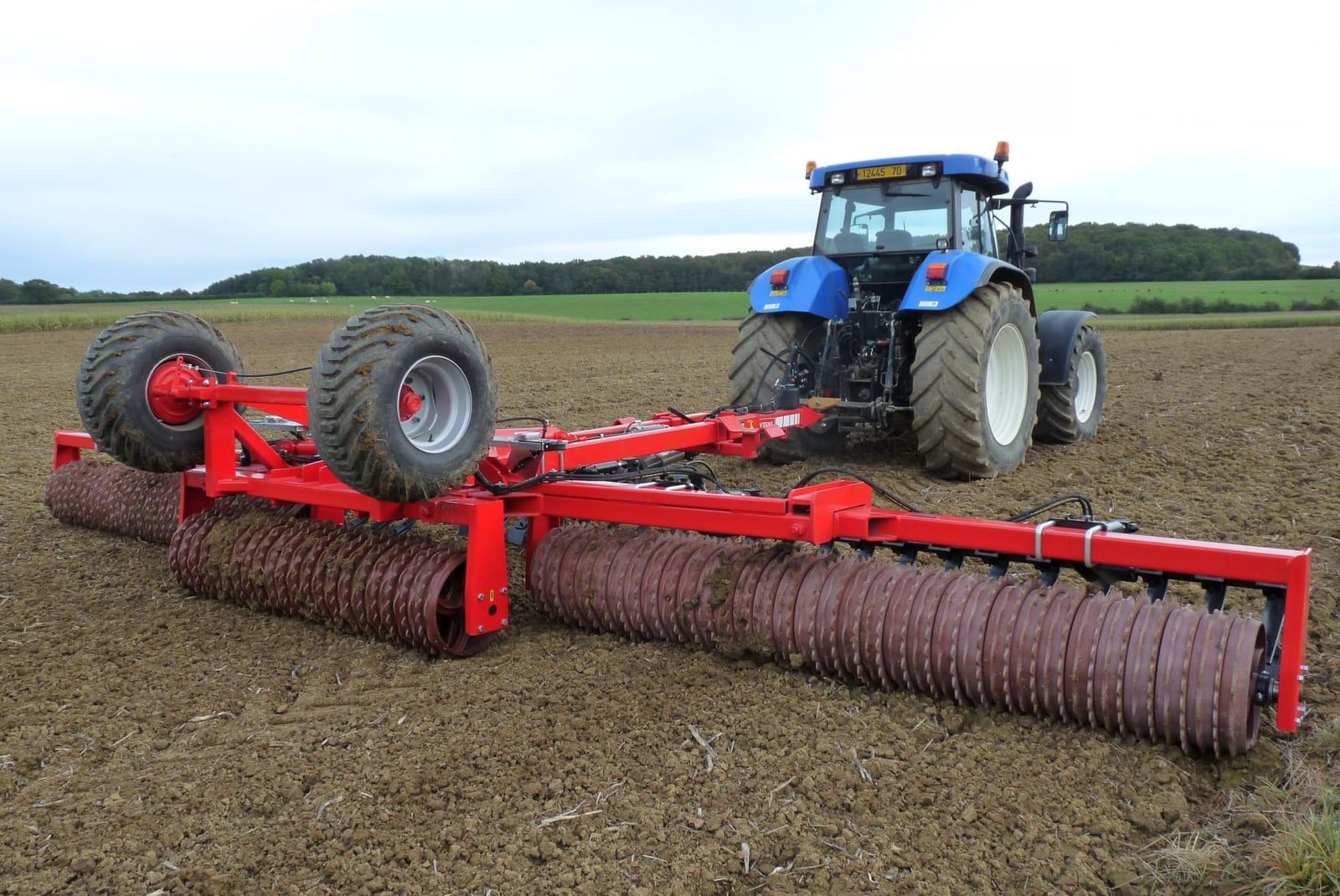 Tracteur New Holland bleu attelé à un rouleau, avant transformation